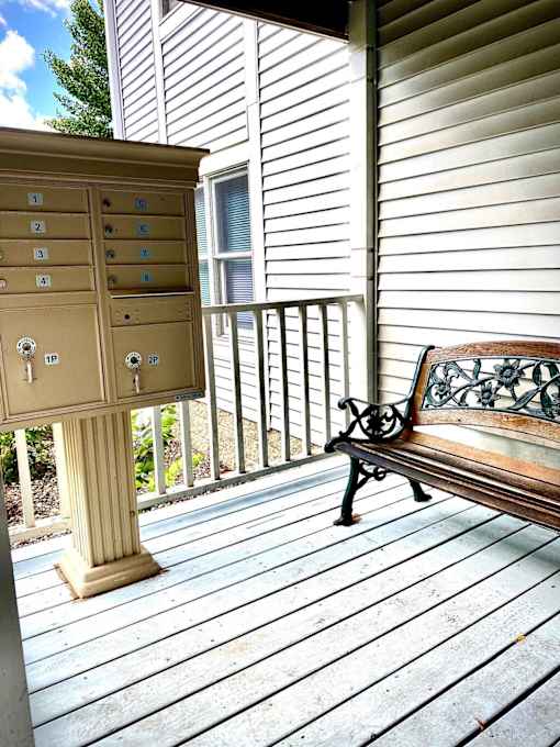 A bench sits on a porch next to a mailbox.