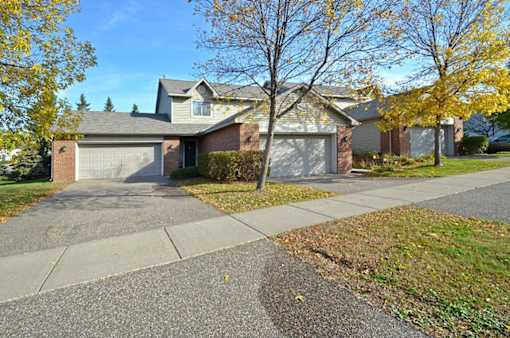 A house with a driveway and a tree with yellow leaves.