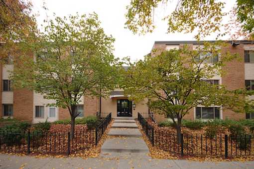 A brick building with a black fence and trees in front.