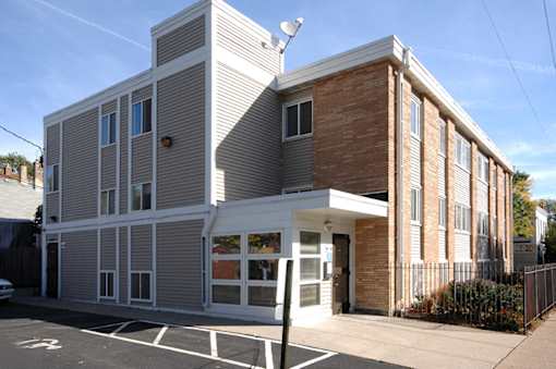 A grey and brown building with a white awning and a black pole in front.