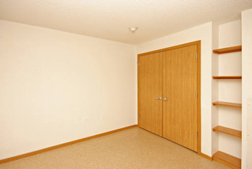 A room with a brown door and a shelf on the wall.