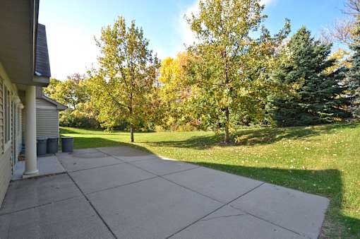 A concrete patio leads to a grassy area with trees.