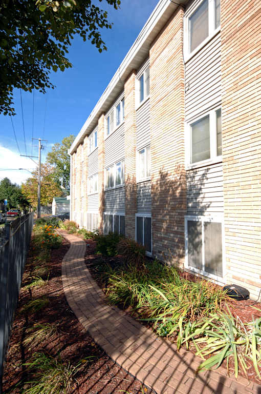 A brick pathway leads to a building with a fence on the left.