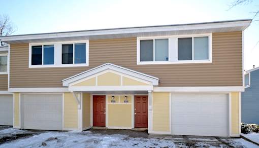 A two-story house with a red door and white garage doors.