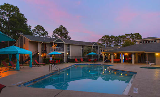 A swimming pool is surrounded by a patio with chairs and umbrellas.