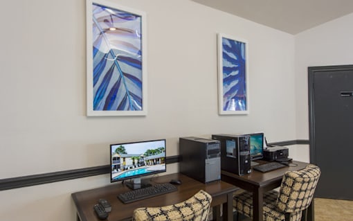 A room with a desk, computer, and two artworks on the wall.