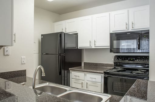 A black refrigerator is in a kitchen with granite countertops and stainless steel appliances.