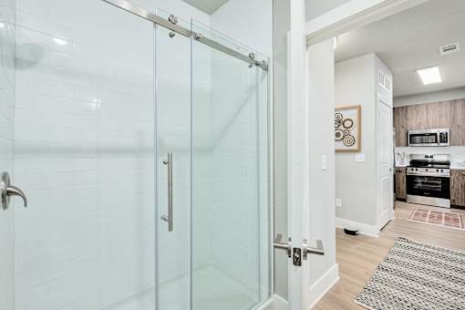 A glass shower door in a white bathroom at The Ashton at East Park Apartments, Kennesaw, 30144