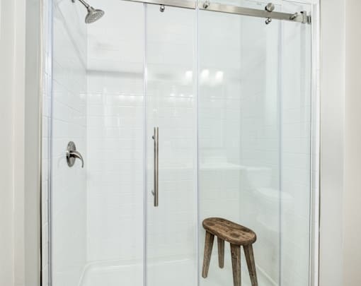 A wooden stool is in front of a glass shower door at The Ashton at East Park Apartments, Georgia, 30144