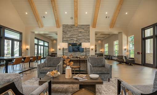A living room with a stone fireplace and wooden beams at The Ashton at East Park Apartments, Kennesaw