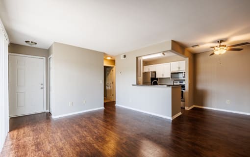 A spacious living room with hardwood floors and a kitchen area in the background.