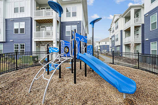 A playground with a blue slide and a black fence.