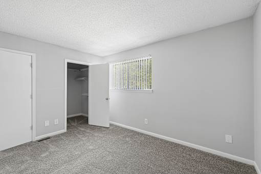 A room with a carpeted floor and a window with blinds.