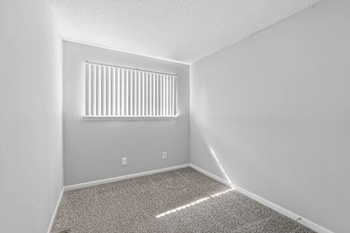 A room with a carpeted floor and a window with blinds.