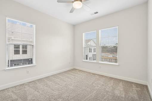 A room with a ceiling fan and two windows with blinds.