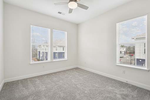 A room with a ceiling fan and two windows with blinds.