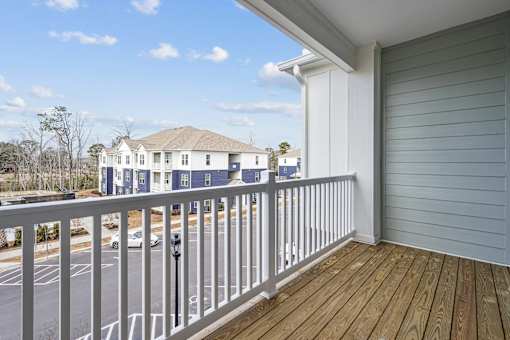 A balcony with a white railing and a wooden floor overlooks a street with cars and houses.