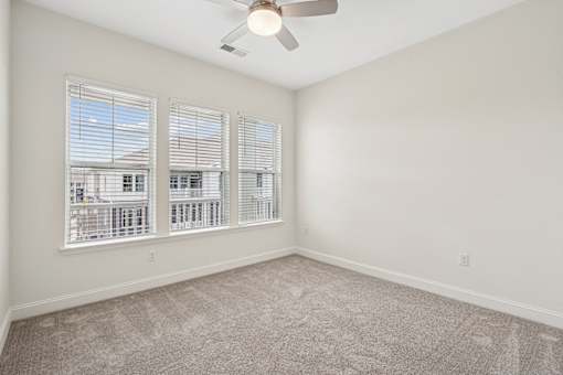 A room with a ceiling fan and a large window with blinds.