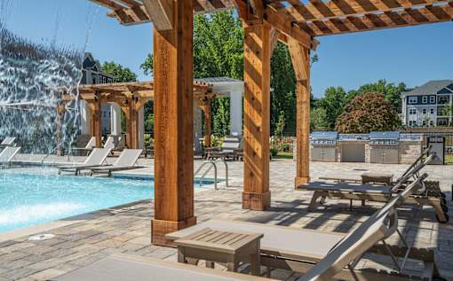 A poolside area with a waterfall and lounge chairs at The Ashton at East Park Apartments, Georgia