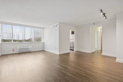 the living room and dining room of an apartment with wood flooring and a window