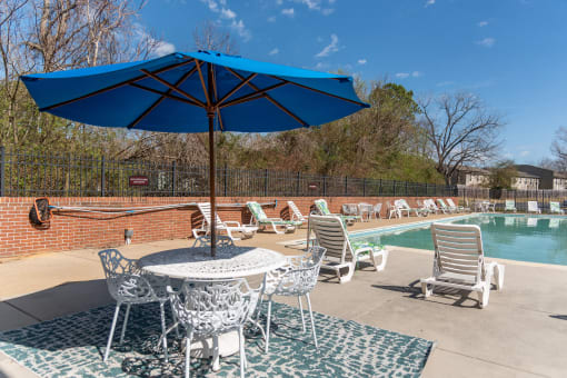 a poolside patio with tables and chairs and an umbrella