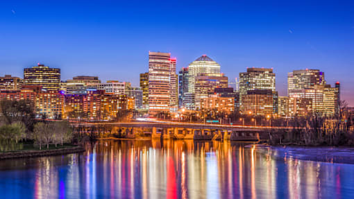 A city skyline at dusk with buildings reflecting in the water.