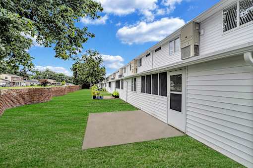 A grassy area in front of a building with a brick wall on the left.