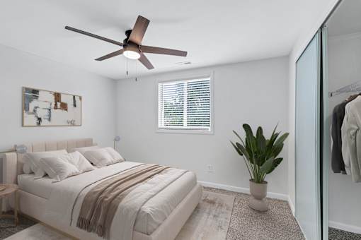A bedroom with a bed, a ceiling fan, and a plant.