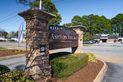 A sign for Ashton Village in front of a parking lot.