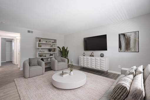 A living room with a grey sofa, a white coffee table, and a television on the wall.