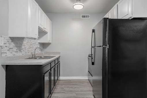 A black refrigerator stands in a kitchen with white cabinets.