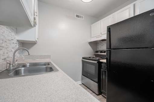 A black refrigerator sits in a kitchen next to a stove and sink.