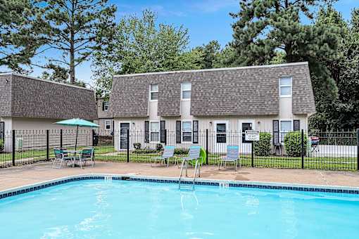 A swimming pool in front of a building with a fence and chairs around it.
