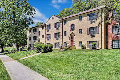 A brick apartment building with a red door and a green lawn in front.