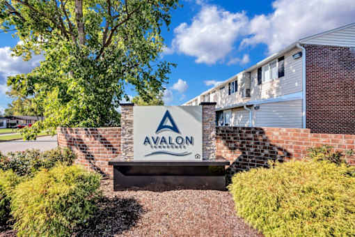 a sign that says avalon apartments in front of a brick wall and trees