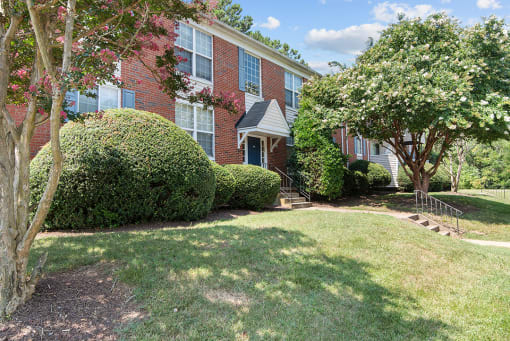 the front of a brick apartment building with a lawn and trees