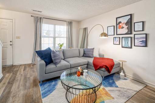 A living room with a grey couch, a glass coffee table, and a red throw blanket.