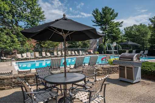 A black umbrella shades a table in a backyard with a pool.