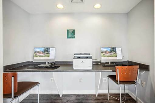 A room with two computer monitors and a printer on a desk.
