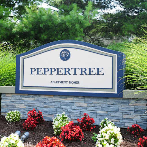 A sign for Peppertree Apartment Homes is surrounded by flowers.