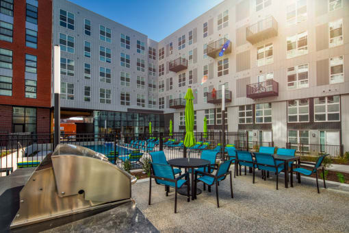 a patio with blue chairs and tables in front of an apartment building