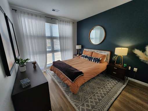 A bedroom with a bed, nightstand, and a round mirror on the wall.
