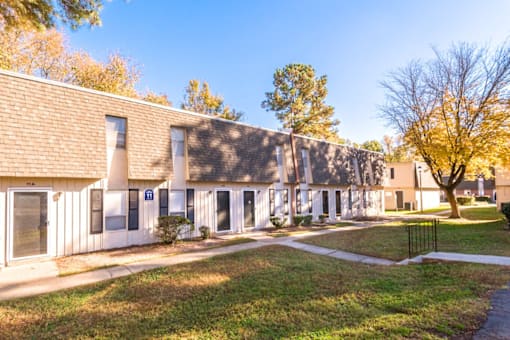 A building with a white facade and a brown roof is surrounded by a grassy area and trees.