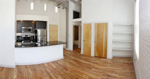 an empty living room with a kitchen and wood floors