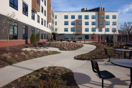 Outdoor seating and walkway area with tables and chairs in front of the apartment building-Beecher Terrace Senior, Louisville, KY