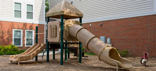 a playground with a slide and a playset in front of a brick building