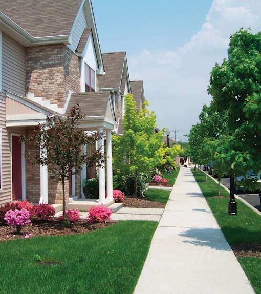A residential street with houses on both sides and a sidewalk in the foreground.