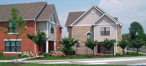 Two houses with a red brick and a tan brick with a tree in front of the house.