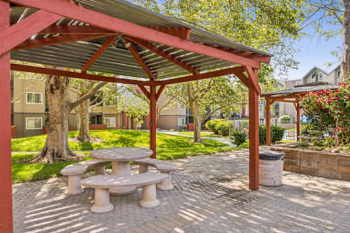 A red and white pavilion with a picnic table in the middle of a brick patio.