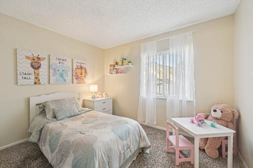 A child's bedroom with a bed, a desk with a teddy bear, and three posters on the wall. at Sarasota South Apartments, Bradenton, FL